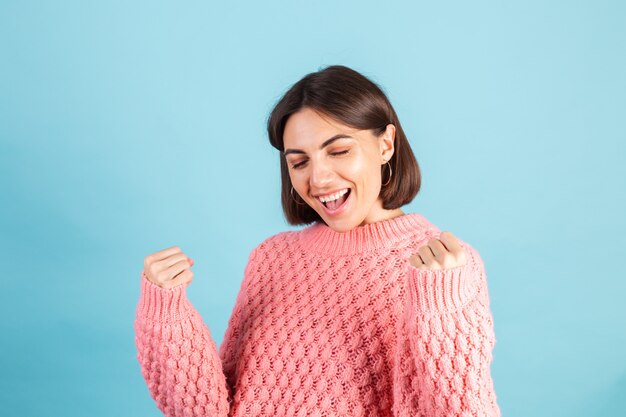 Jonge brunette in warme roze trui geïsoleerd op blauwe muur