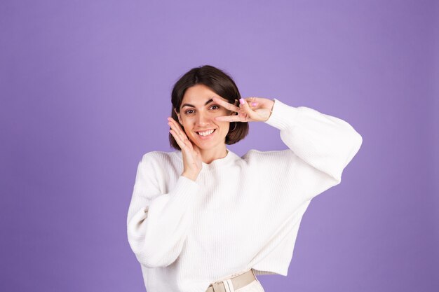 Jonge brunette in witte casual trui geïsoleerd op paarse muur