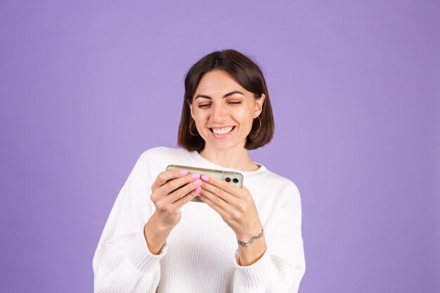 Jonge brunette in witte casual trui geïsoleerd op paarse muur