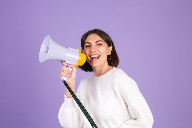 Jonge brunette in witte casual trui geïsoleerd op paarse muur