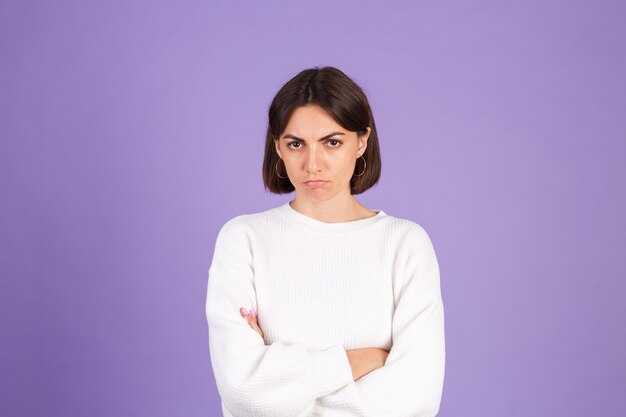 Jonge brunette in witte casual trui geïsoleerd op paarse muur