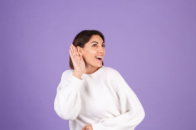 Jonge brunette in witte casual trui geïsoleerd op paarse muur