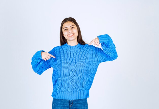 Jonge brunette meisje in blauwe trui wijzen iets op wit.