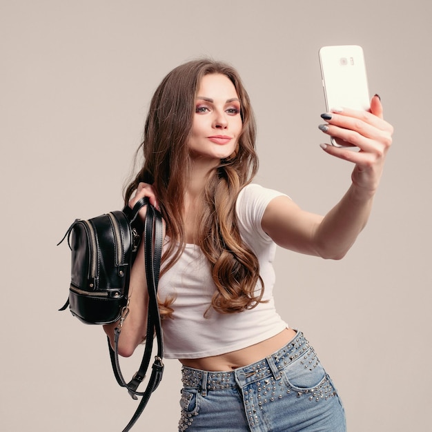 Jonge brunette meisje met krullend haar met kleine rugzak en smartphone
