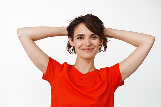 Jonge brunette meisje rust, hand in hand achter het hoofd en ontspannen, liggend met de handen achter het hoofd, staande op een witte achtergrond.