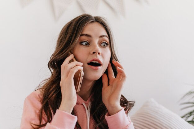 Jonge brunette met mooie ogen en verbaasde gezichtsuitdrukking communiceert op haar mobiele apparaat