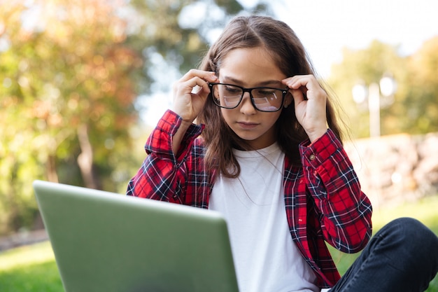 Jonge brunette schoolmeisje zitten buiten met laptopcomputer