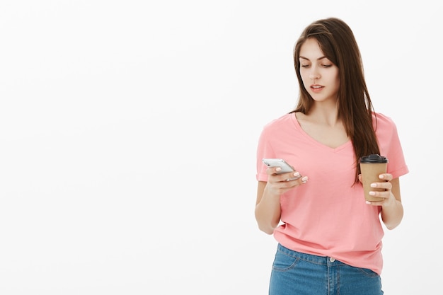 Jonge brunette vrouw poseren in de studio met haar telefoon en koffie