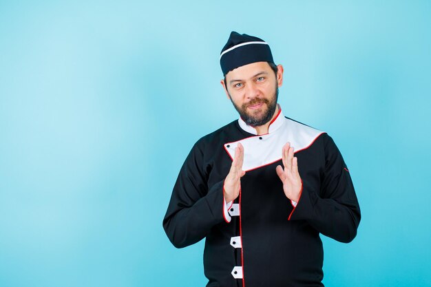 Jonge chef-kok kijkt naar de camera door zijn handen op een blauwe achtergrond te houden
