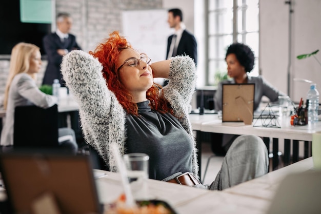Jonge creatieve zakenvrouw met handen achter het hoofd die een pauze neemt en met gesloten ogen op kantoor rust