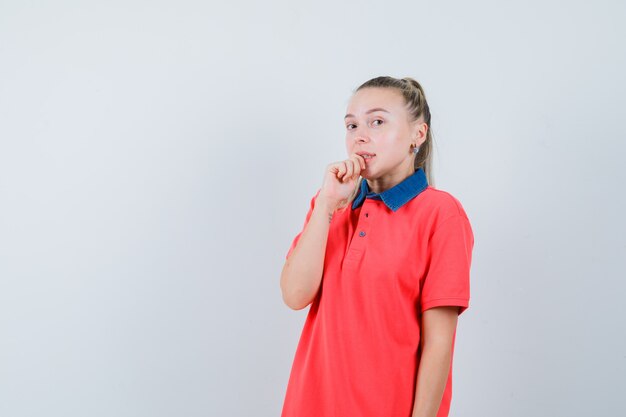 Jonge dame bijt vinger in t-shirt en kijkt beschaamd. vooraanzicht.