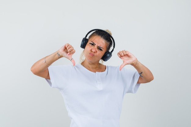 Jonge dame die aan muziek luistert, dubbele duimen neer in t-shirt, vooraanzicht toont.