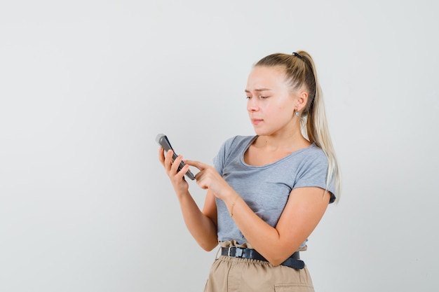 Jonge dame die calculator in t-shirt en broek gebruikt en bezig kijkt