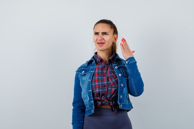 Jonge dame die de hand opsteekt in een verbaasd gebaar terwijl ze opkijkt in shirt, jas en ontevreden kijkt, vooraanzicht.