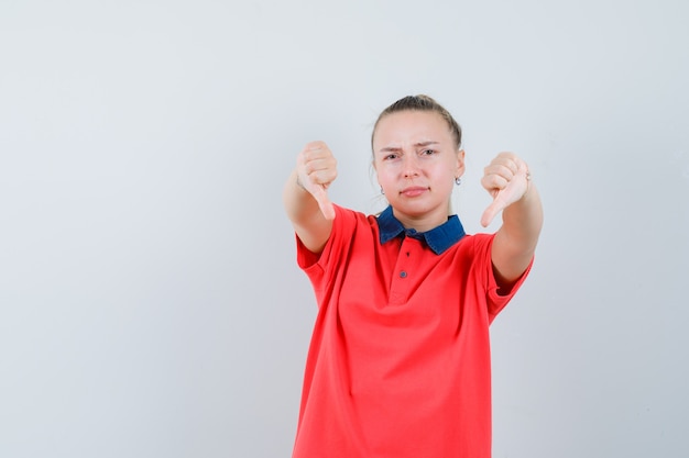 Jonge dame die dubbele duimen neer in t-shirt toont en ontevreden kijkt