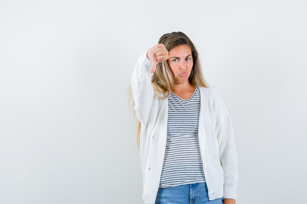 Jonge dame die duim neer in t-shirt, jasje toont en teleurgesteld, vooraanzicht kijkt.