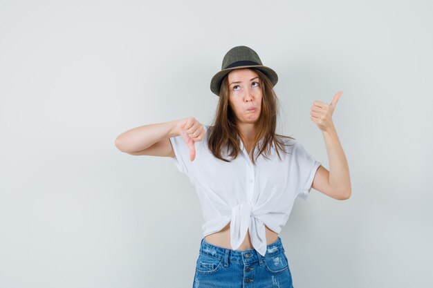 Jonge dame die duimen op en neer in de hoed van de t-shirtjeans toont en aarzelend kijkt