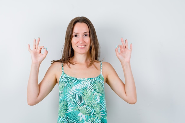 Jonge dame die een goed gebaar in blouse toont en er gelukkig uitziet, vooraanzicht.