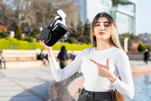 Jonge dame die een virtual reality-bril vasthoudt en er met de vinger op wijst Foto van hoge kwaliteit