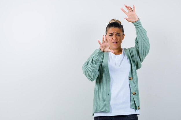 Jonge dame die haar handen in de verdediging houdt, poseert in t-shirt, jas en ziet er bang uit