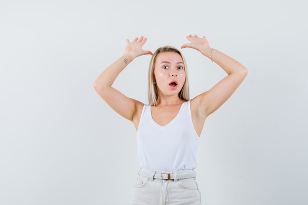 Jonge dame die haar handen in witte blouse opheft en gealarmeerd kijkt