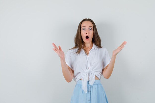 Jonge dame die haar handen met open handpalmen in blouse, rok opheft en gealarmeerd kijkt