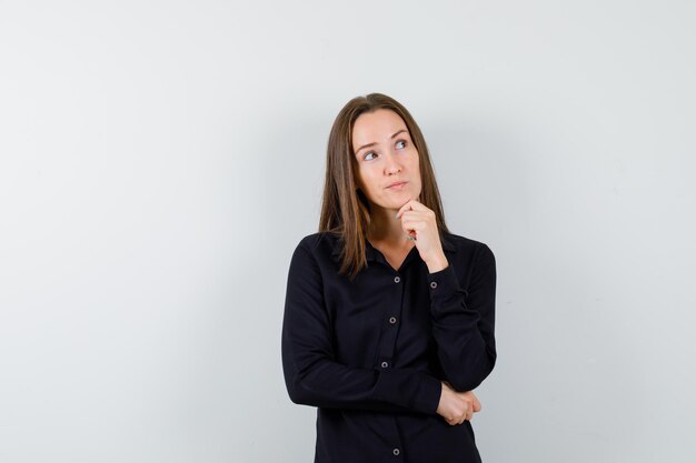 Jonge dame die haar kin op de hand houdt en peinzend kijkt