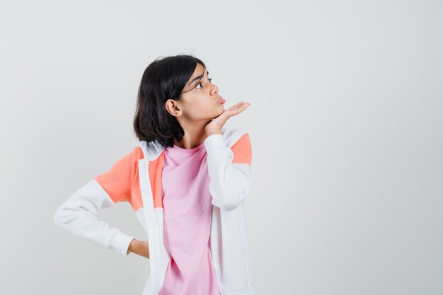 Jonge dame die hand naar haar kaak houdt terwijl ze opzij kijkt in jasje, roze shirt en er raar uitziet.