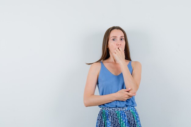 Jonge dame die hand op haar mond in blouse, rok houdt en bang, vooraanzicht kijkt.