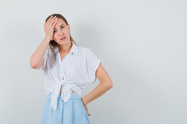 Jonge dame die hand op hoofd in blouse en rok houdt en vergeetachtig kijkt