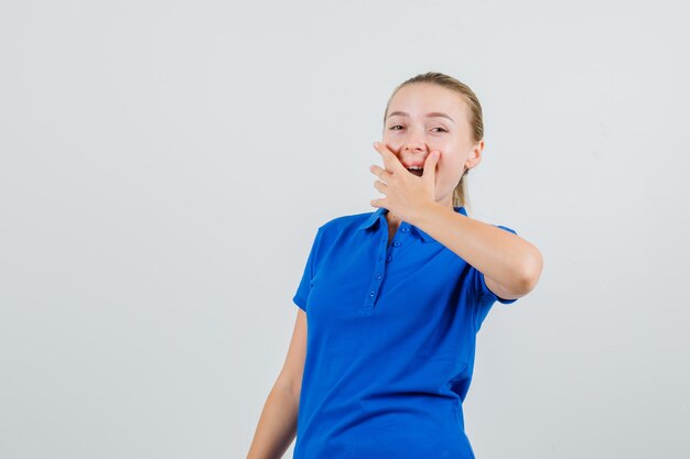 Jonge dame die hand op mond in blauw t-shirt houdt en gelukkig kijkt