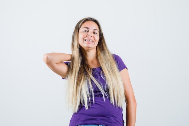 Jonge dame die hand op nek in violet t-shirt houdt en er mooi uitziet. vooraanzicht.