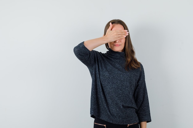 Jonge dame die hand op ogen in overhemd houdt en optimistisch kijkt