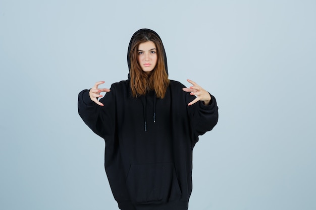 Gratis foto jonge dame die handen op agressieve manier in oversized hoodie, broek houdt en geïrriteerd kijkt. vooraanzicht.