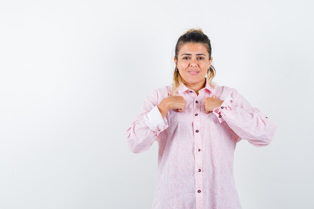 Jonge dame die handen op borst in roze overhemd houdt en vrolijk kijkt