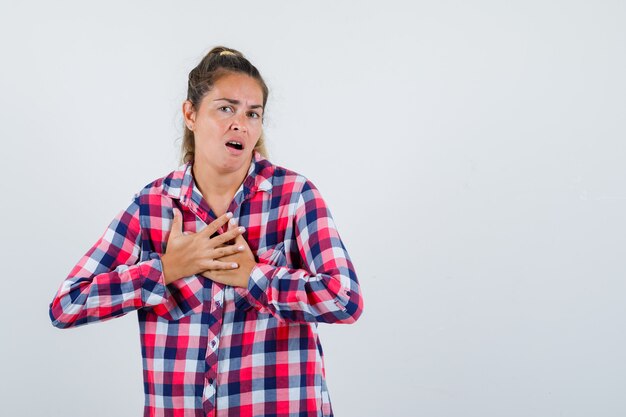 Gratis foto jonge dame die handen op de borst houdt in geruit overhemd en pijnlijk, vooraanzicht kijkt.