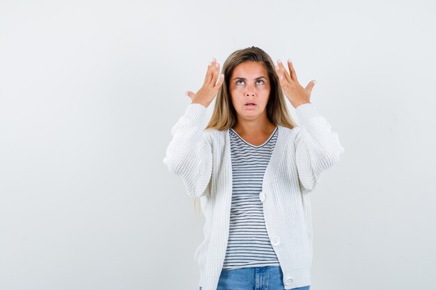 Jonge dame die handen opheft terwijl het opzoeken in t-shirt, jasje en peinzend kijkt. vooraanzicht.