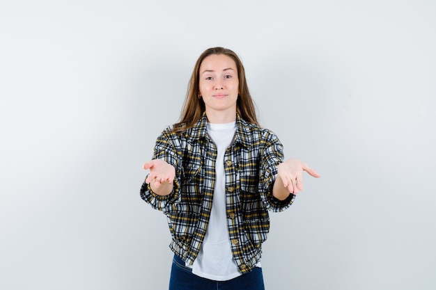 Jonge dame die handpalm uitspreidt in t-shirt, jasje, spijkerbroek en op zoek hulpeloos, vooraanzicht.