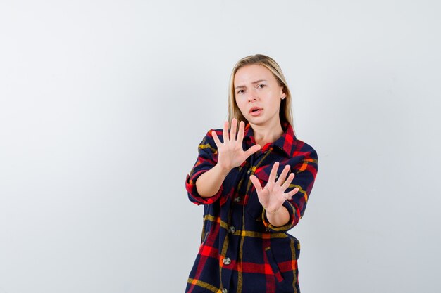 Jonge dame die handpalmen in overgave gebaar in geruit overhemd toont en bang, vooraanzicht kijkt.