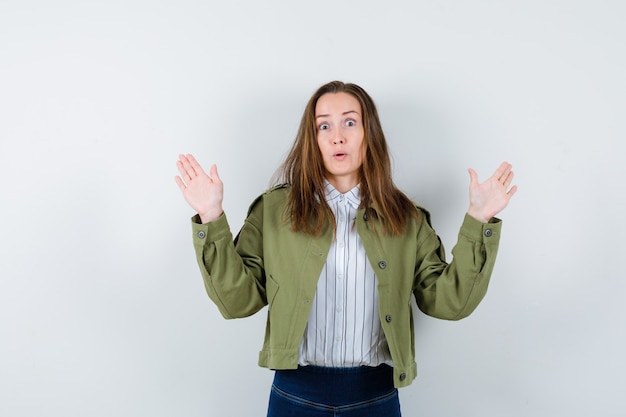 Gratis foto jonge dame die handpalmen toont in overgavegebaar in shirt, jas en er bang uitziet, vooraanzicht.