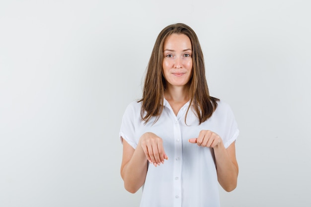 Jonge dame die het gebaar van de kattenpoot in witte blouse toont en grappig kijkt.