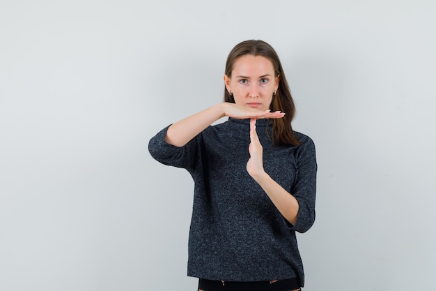 Jonge dame die het gebaar van de tijdonderbreking in overhemd toont en ernstig kijkt