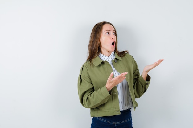 Jonge dame die iets hierboven in blouse, jas laat zien en er verrast uitziet.