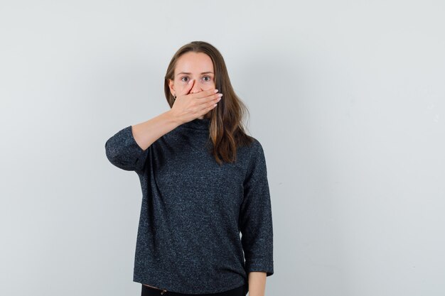 Jonge dame die in overhemd hand op mond houdt en kalm kijkt