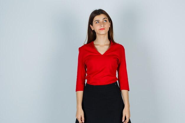 Jonge dame die in rode blouse, rok en peinzend kijkt
