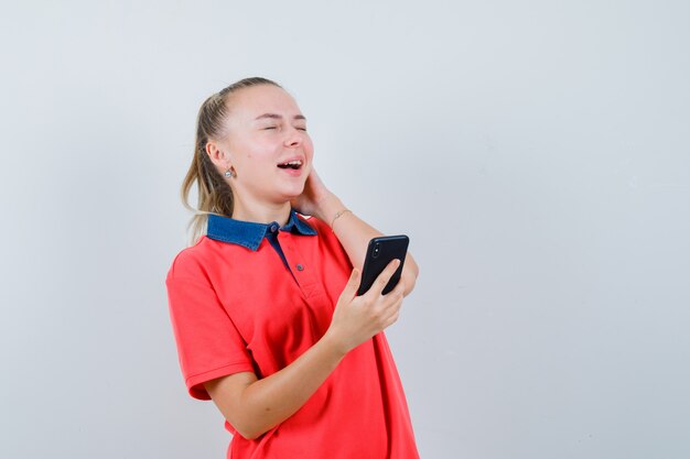 Jonge dame die in t-shirt mobiele telefoon houdt en gelukkig kijkt