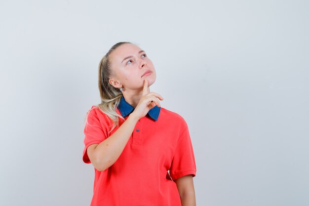 Jonge dame die in t-shirt omhoog kijkt en nadenkend kijkt