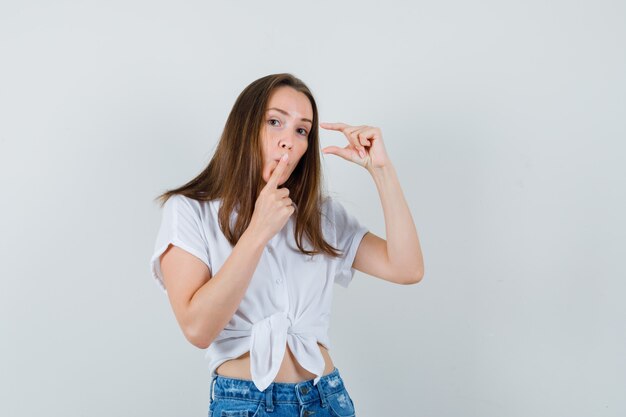 Jonge dame die klein formaat in witte blouse toont en stil kijkt. vooraanzicht.