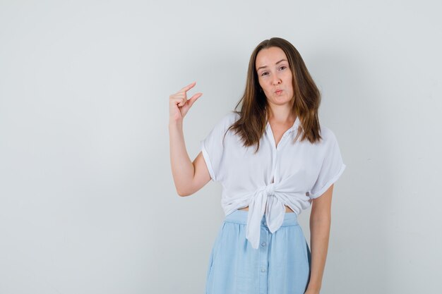 Jonge dame die klein grootteteken in blouse en rok toont en er zelfverzekerd uitziet