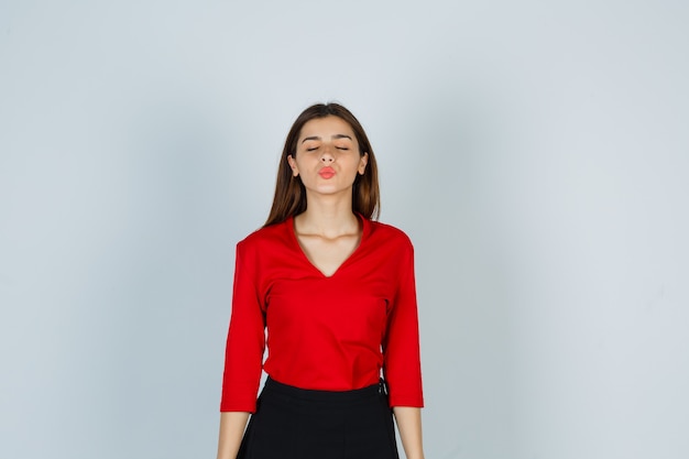 Jonge dame die kus met pruilende lippen in rode blouse, rok verzendt en er schattig uitziet